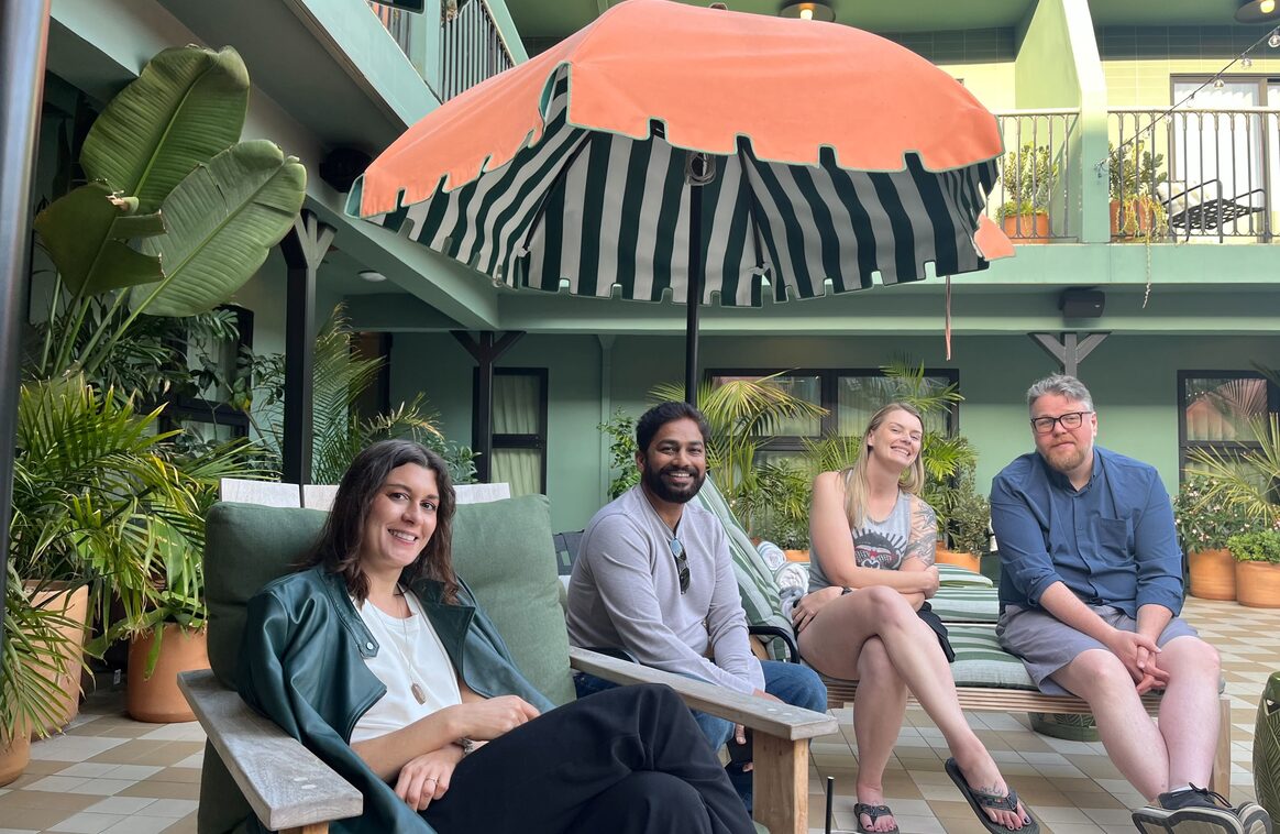 Four Updater colleagues seated together under a striped umbrella at a team offsite
