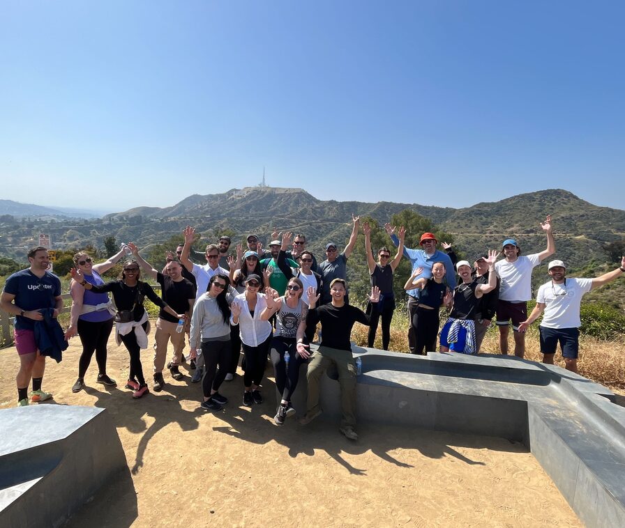 Updater teammates waving from a hilltop trail overlooking a valley