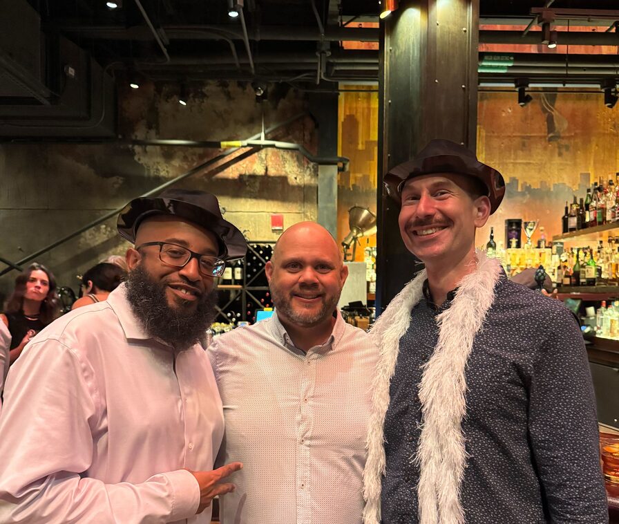 Three Updater colleagues in festive hats and a feather boa, arms around each other at a bar