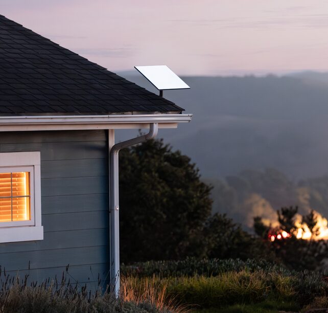 A Starlink dish mounted on the roof of a house overlooking open hills at dusk