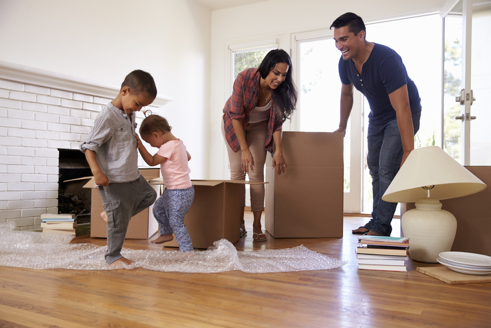Children walking on bubble wrap while their parents pack moving boxes