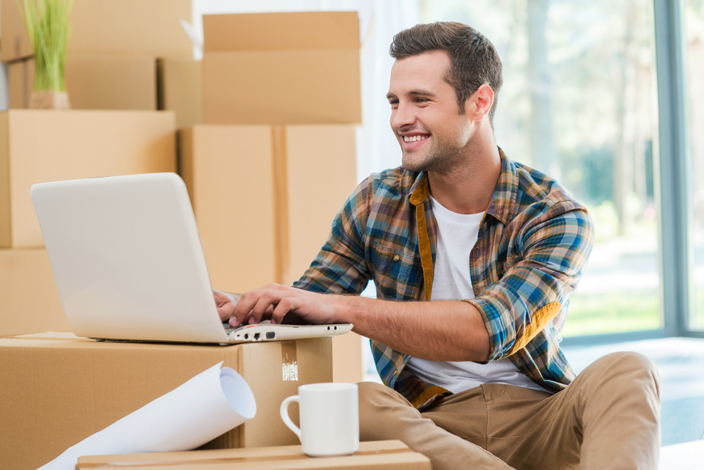 Recent graduate using laptop on packed moving boxes